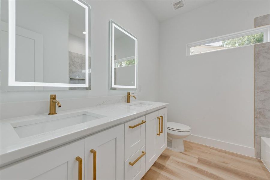 Bathroom with toilet, a healthy amount of sunlight, double sink vanity, and wood-type flooring