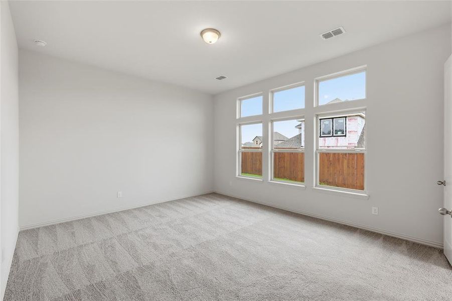 Spacious room featuring multiple large windows, neutral gray patterned carpet, and a light-toned ceiling with a flush-mount fixture Spacious room featuring multiple large windows, neutral gray patterned carpet, and a light-toned ceiling with a flush-mount fixture