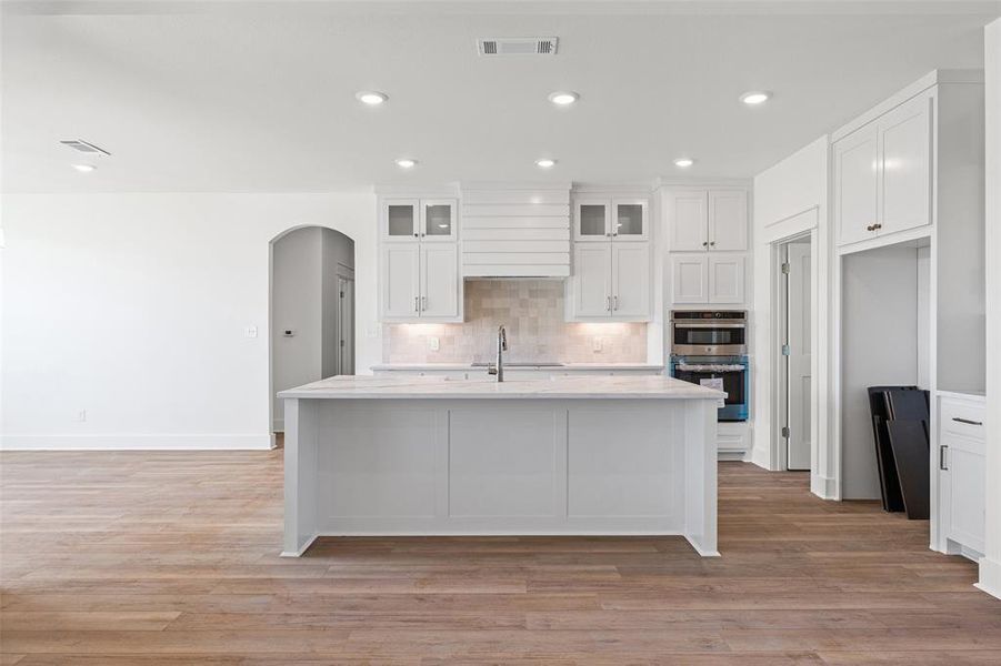 Modern kitchen featuring a central island, white cabinetry, integrated stainless steel appliances, a tile backsplash, and recessed lighting