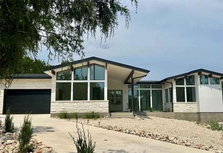 Rear view of house with stone siding, driveway, an attached garage, and a patio Rear view of house with stone siding, driveway, an attached garage, and a patio
