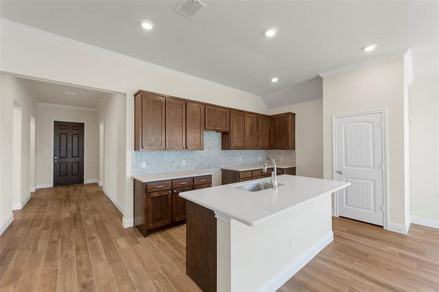 Kitchen featuring backsplash, ornamental molding, a kitchen island with sink, sink, and light hardwood / wood-style floors