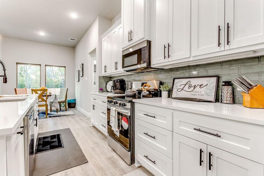 Kitchen featuring sink, stainless steel appliances, decorative backsplash, white cabinets, and light wood-type flooring