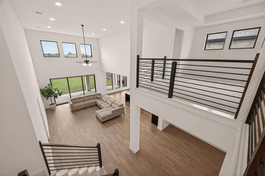 This spacious, modern living room features an open floor plan with high ceilings and abundant natural light. It offers a view of the outdoors through large windows and sliding glass doors, and includes a stylish, comfortable sectional sofa. The wood flooring adds warmth, while the contemporary railing and staircase provide a sleek touch.
