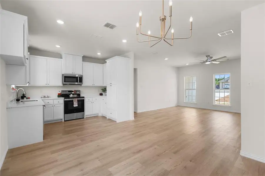 Kitchen featuring white cabinetry, stainless steel appliances, a chandelier, light wood finished floors, and recessed lighting