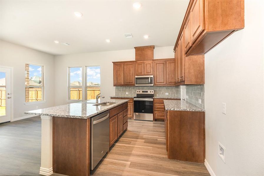Kitchen featuring decorative backsplash, light wood-style flooring, appliances with stainless steel finishes, a sink, and brown cabinetry