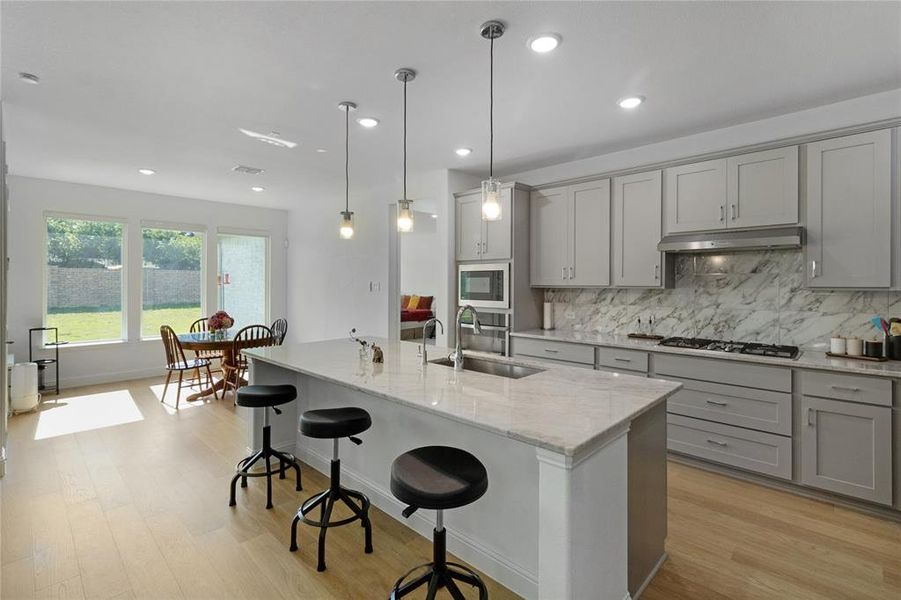 Contemporary kitchen featuring light gray cabinetry, a gas cooktop, built-in microwave, and a large central island with an integrated sink