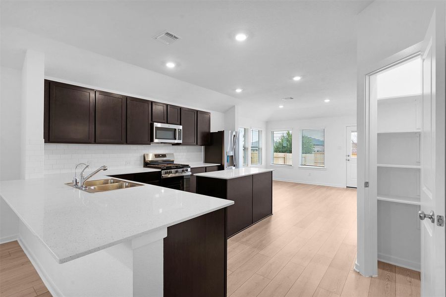Kitchen featuring dark brown cabinetry, a kitchen island, stainless steel appliances, light stone countertops, and a peninsula