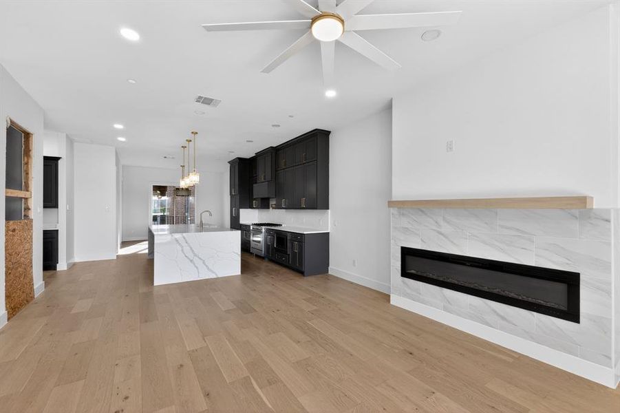 Unfurnished living room with a tile fireplace, light wood-style floors, a ceiling fan, and a chandelier