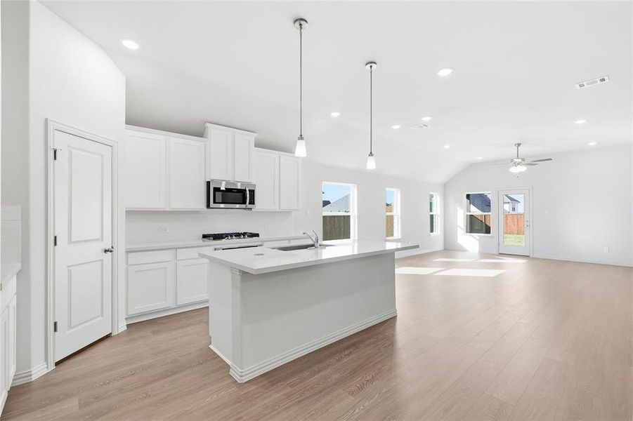 Kitchen featuring decorative light fixtures, vaulted ceiling, white cabinetry, a kitchen island with sink, and light wood-style flooring Kitchen featuring decorative light fixtures, vaulted ceiling, white cabinetry, a kitchen island with sink, and light wood-style flooring