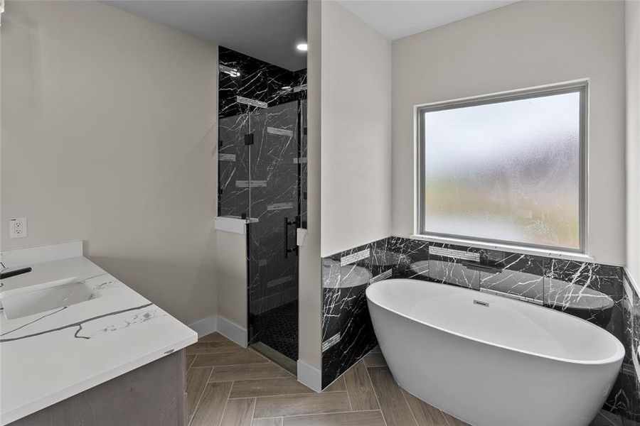 Bathroom featuring tile walls, a marble finish shower, a freestanding tub, vanity, and wainscoting