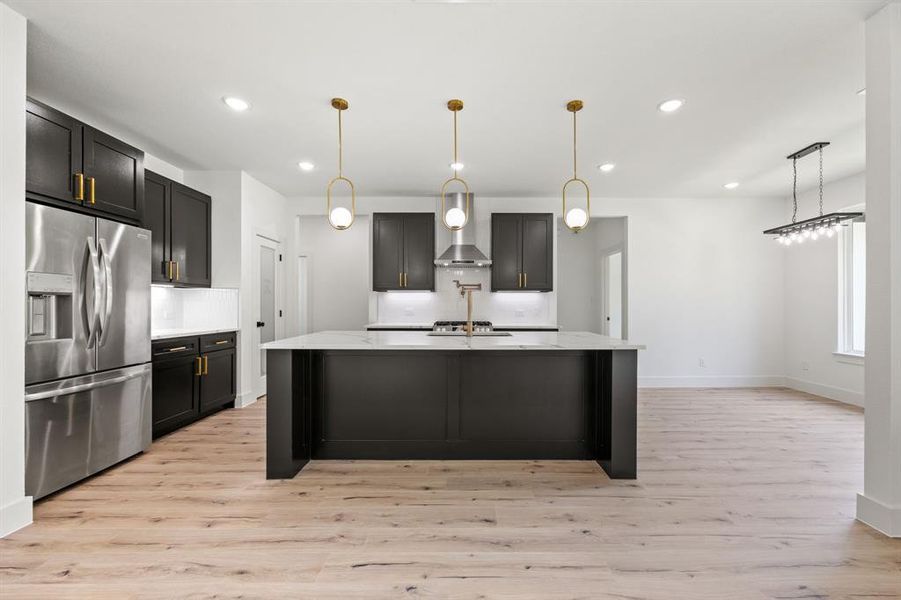 Kitchen with stainless steel fridge, wall chimney range hood, recessed lighting, light wood-style flooring, and baseboards Kitchen with stainless steel fridge, wall chimney range hood, recessed lighting, light wood-style flooring, and baseboards