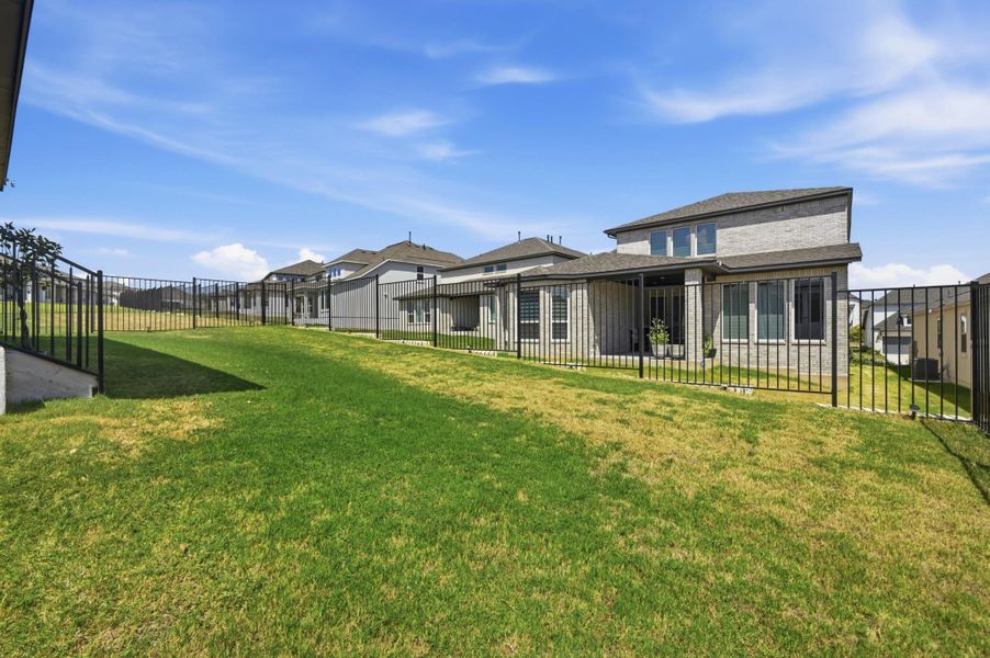 An expansive green lawn slopes gently upward along a secure metal boundary fence.