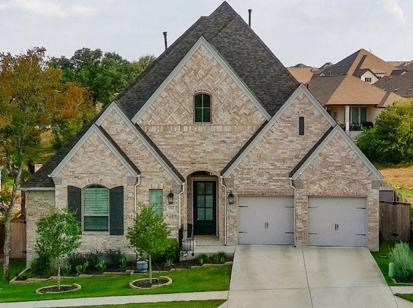 French country inspired facade with brick siding, concrete driveway, a shingled roof, and a front lawn French country inspired facade with brick siding, concrete driveway, a shingled roof, and a front lawn