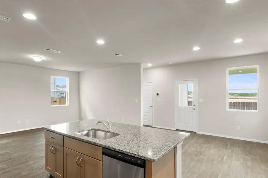 Kitchen featuring stainless steel dishwasher, light wood-type flooring, a kitchen island with sink, light stone countertops, and recessed lighting