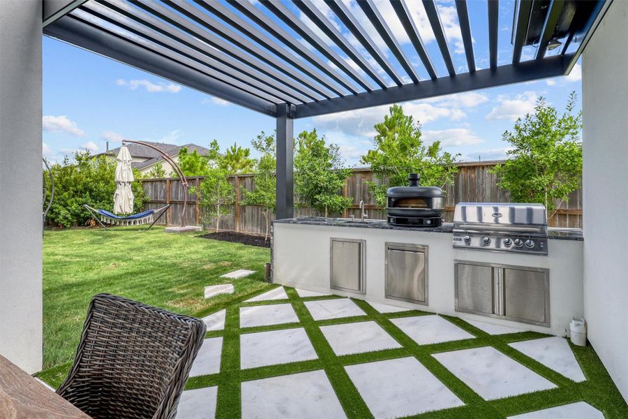 Outdoor kitchen is finished with sparkling white travertine tiles, granite countertops, gas grill, pizza oven, and sink. The area opens up to a landscaped green space. Enjoy complete privacy, with no neighbor behind or beside the property.