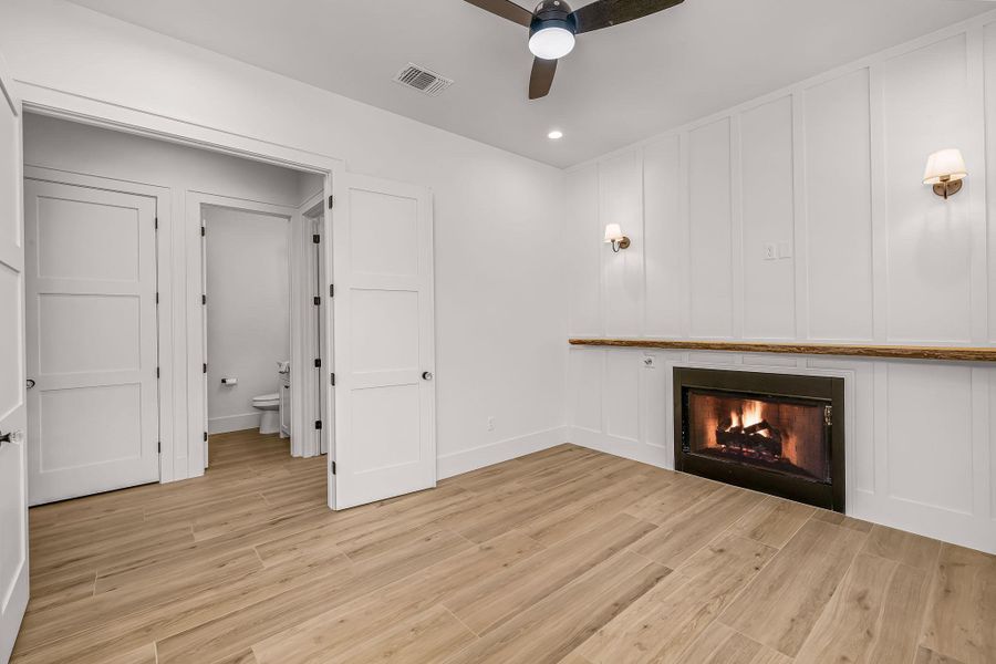 Unfurnished living room featuring a warm lit fireplace, light wood finished floors, visible vents, and a decorative wall