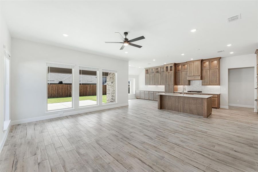 Open-concept living area and kitchen with wood-look tile floors, brown cabinets, center island, and sliding glass doors to backyard patio.