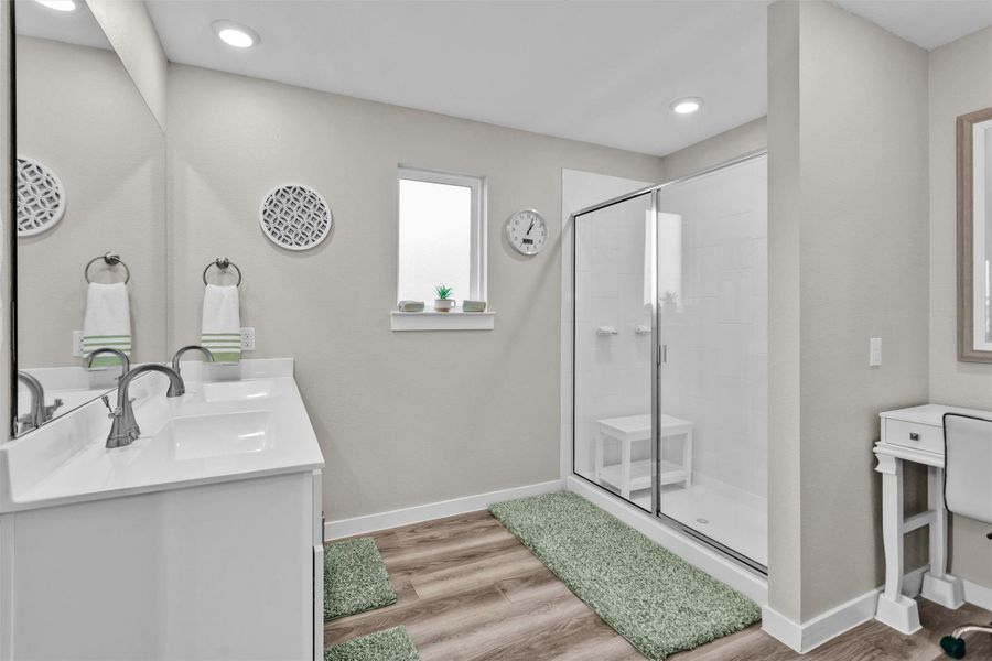 This modern bathroom features a spacious glass-enclosed shower, dual sinks with sleek fixtures, and stylish decor. The room is bright and airy, with light walls and wood-style flooring.