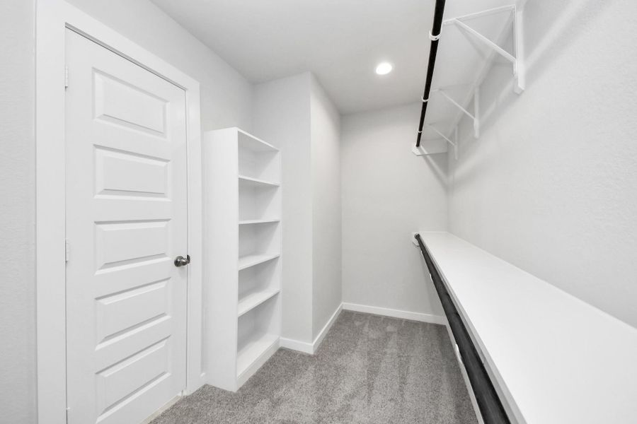 Experience luxury in this spacious walk-in closet with high ceilings and plush carpet. Warm paint tones, built-in shelving, and dark finishes create a contemporary and functional retreat. Sample photo of completed home with similar floor plan. Actual colors and selections may vary. Experience luxury in this spacious walk-in closet with high ceilings and plush carpet. Warm paint tones, built-in shelving, and dark finishes create a contemporary and functional retreat. Sample photo of completed home with similar floor plan. Actual colors and selections may vary.