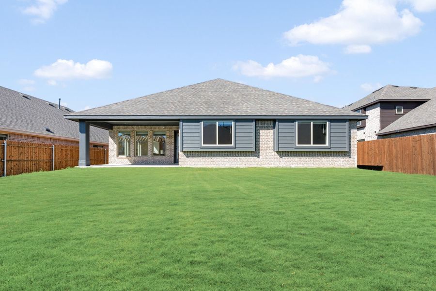 Rear view of single-story brick home with gray siding, large windows, and spacious fenced backyard lawn