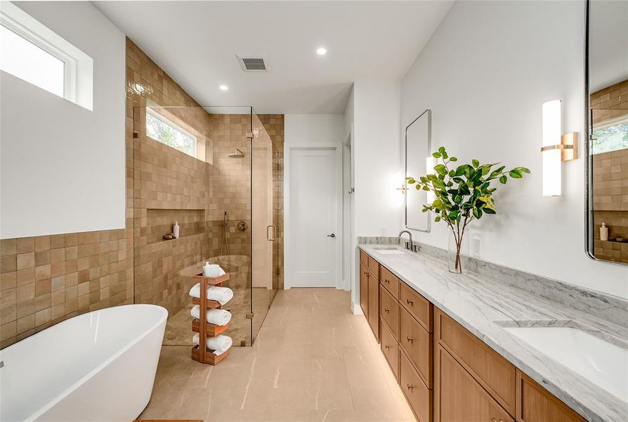 Spacious bathroom featuring a freestanding soaking tub, a frameless glass shower enclosure with built-in niches, a dual vanity with undermount sinks, and a stone countertop