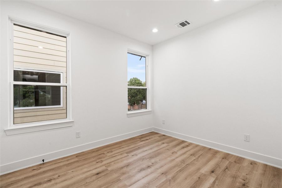 Generous windows invite natural light from multiple angles, giving this secondary bedroom a bright, open feel. Oak-colored flooring and crisp white walls create a serene foundation—ready to adapt as a guest suite, office, or creative retreat.