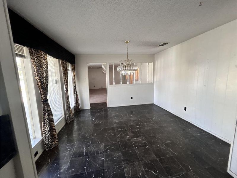 Unfurnished dining area with a textured ceiling, a chandelier, and dark marble finish floors Unfurnished dining area with a textured ceiling, a chandelier, and dark marble finish floors