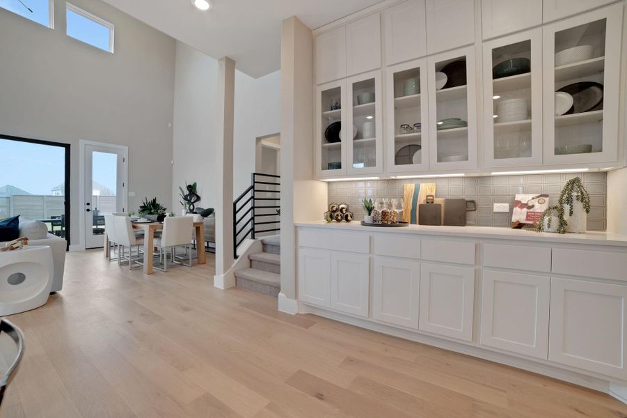 Bar area featuring white cabinets, a high ceiling, glass fronted cabinets, light wood-style floors, and tasteful backsplash