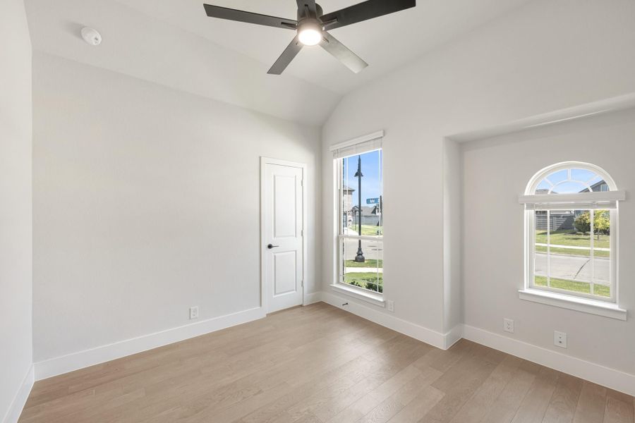 Empty bedroom with vaulted ceiling, ceiling fan, hardwood floors, and two windows with natural light
