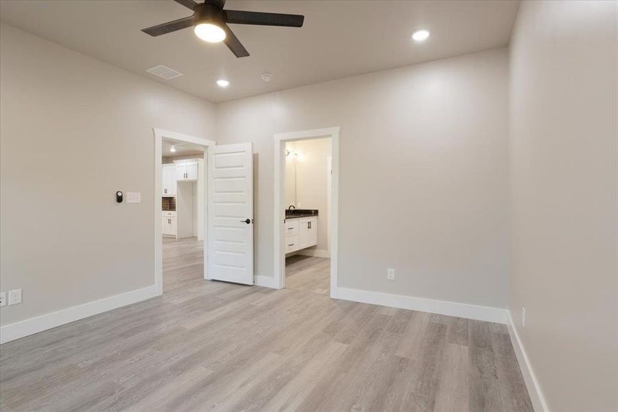 Unfurnished bedroom with connected bathroom, light hardwood / wood-style flooring, and ceiling fan