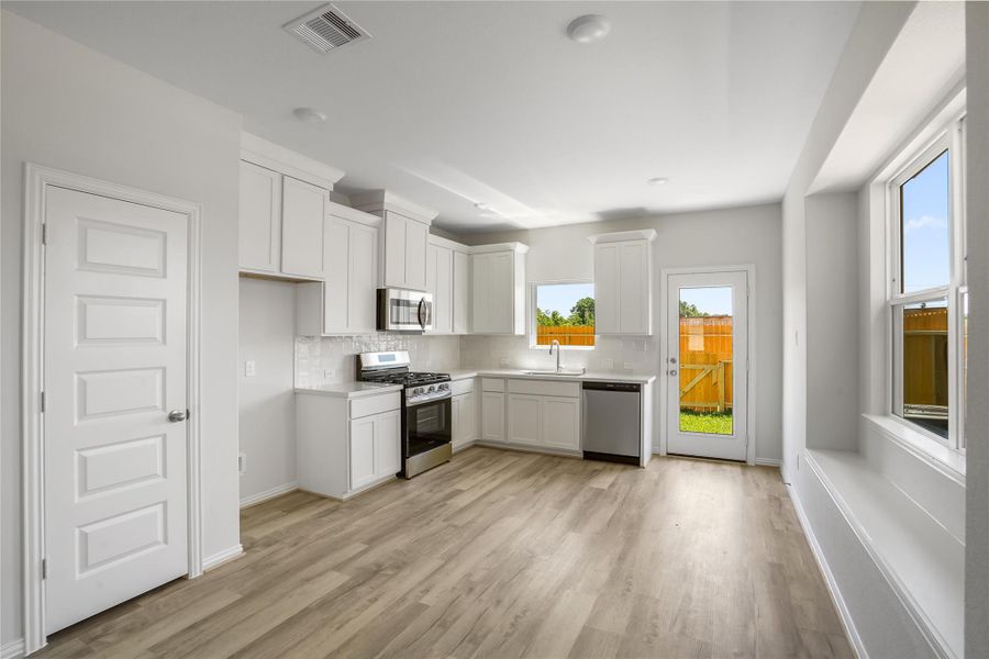 The kitchen features large windows, access to the backyard, stainless steel appliances, white cabinets, and tile backsplash.