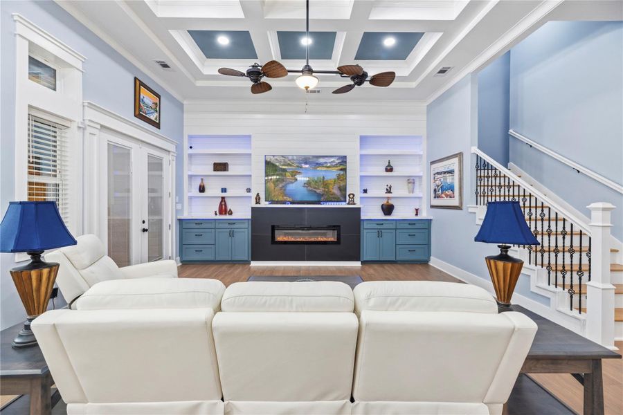 Family room highlighted by soaring coffered ceilings, custom built-ins, and a sleek linear fireplace designed for sophisticated comfort.