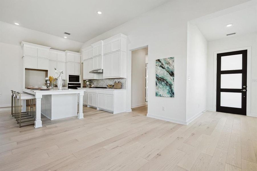 Kitchen with a center island with sink, white cabinets, light hardwood / wood-style floors, a kitchen bar, and stainless steel appliances