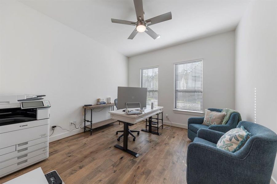 The study is enhanced with a sleek, modern ceiling fan and large windows that overlook the front of the home, filling the space with natural light.