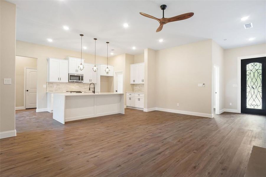 Kitchen with hardwood / wood-style floors, backsplash, decorative light fixtures, an island with sink, and ceiling fan