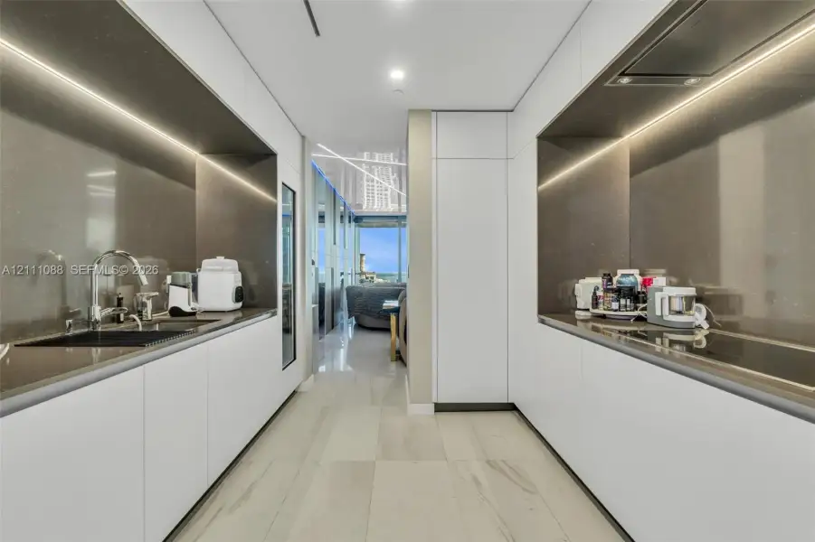 Contemporary kitchen featuring white flat-panel cabinetry, solid-surface countertops, integrated under-cabinet lighting, a built-in cooktop, and large-format tile flooring Contemporary kitchen featuring white flat-panel cabinetry, solid-surface countertops, integrated under-cabinet lighting, a built-in cooktop, and large-format tile flooring