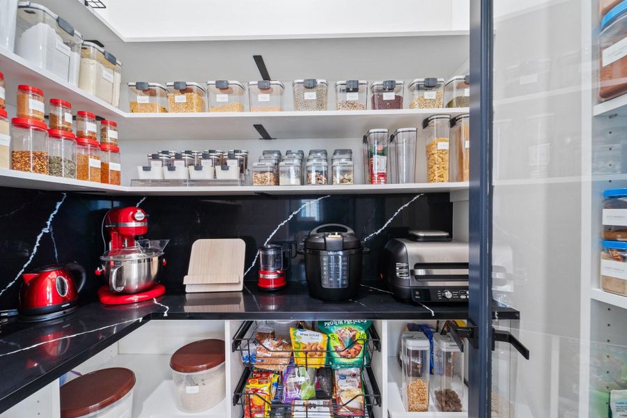 This walk-in pantry combines style and function, with sleek black countertops and ample shelving. Pull-out drawers provide easy access, creating an organized, efficient storage space that enhances the kitchen’s overall design. This walk-in pantry combines style and function, with sleek black countertops and ample shelving. Pull-out drawers provide easy access, creating an organized, efficient storage space that enhances the kitchen’s overall design.