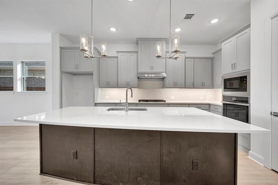 Kitchen with an island with sink, gray cabinets, light wood finished floors, and light stone counters Kitchen with an island with sink, gray cabinets, light wood finished floors, and light stone counters