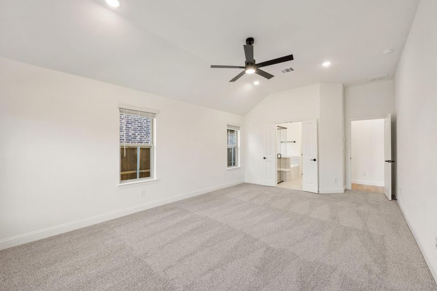 Empty master bedroom with vaulted ceiling, ceiling fan, gray carpet, and open walk-in closet doorway Empty master bedroom with vaulted ceiling, ceiling fan, gray carpet, and open walk-in closet doorway