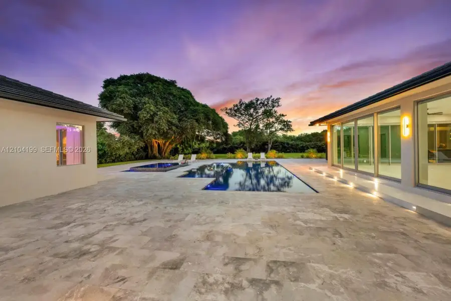 Expansive stone patio featuring an in-ground pool, integrated spa, and floor-to-ceiling glass wall panels