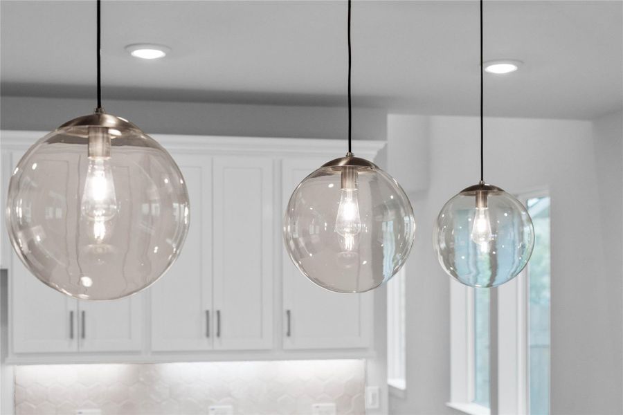 Three exquisite, clear glass pendant lights that elegantly hang above the kitchen island, providing focused task lighting and a touch of refined style.