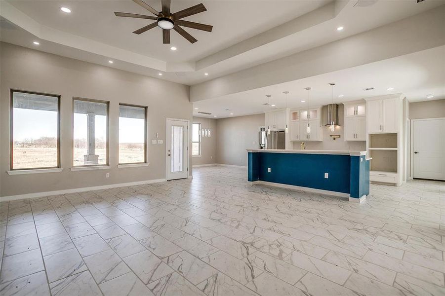 Unfurnished living room with ceiling fan, a high ceiling, and a tray ceiling