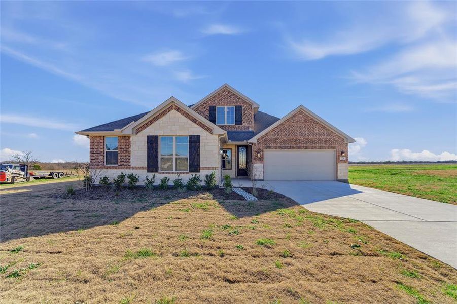 View of front of property featuring brick siding, driveway, a garage, stone siding, and a front lawn