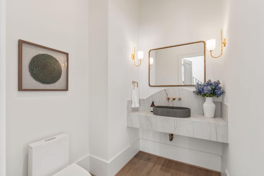 The powder bath showcases a custom floating vanity with a stone surround and a vessel sink. Wall-mounted fixtures and elegant lighting add a refined, designer touch.