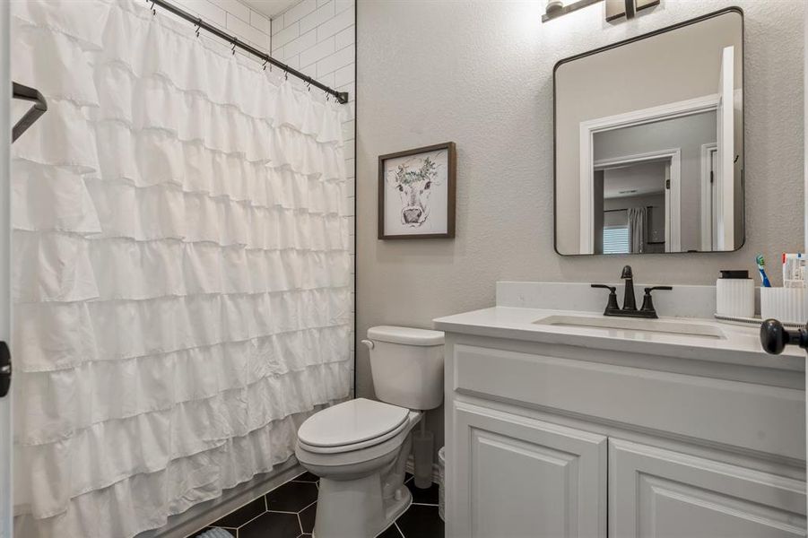 Downstairs bathroom featuring vanity, a textured wall, dark tile patterned floors, and a shower with shower curtain Downstairs bathroom featuring vanity, a textured wall, dark tile patterned floors, and a shower with shower curtain