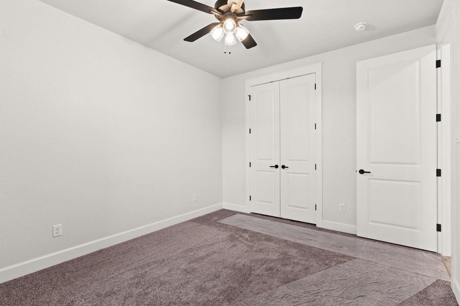 Unfurnished bedroom with dark colored carpet, a closet, and ceiling fan Unfurnished bedroom with dark colored carpet, a closet, and ceiling fan