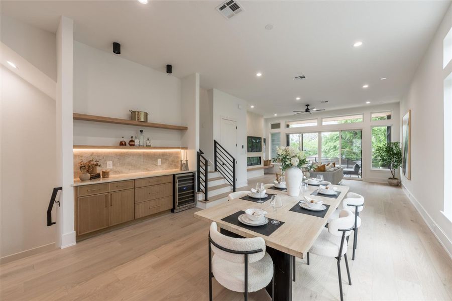 The main living level reimagined: lifted to the second floor to capture light, breeze, and a treetop view that ground-floor plans can't offer. A built-in oak bar stretches the sidewall, a stone slab backsplash rising full-height behind floating shelves that glow from below with integrated LED.