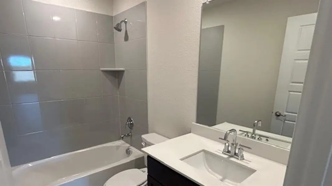 Full bathroom featuring a tub and shower combination with gray tile surround, chrome fixtures, and a corner shelf
