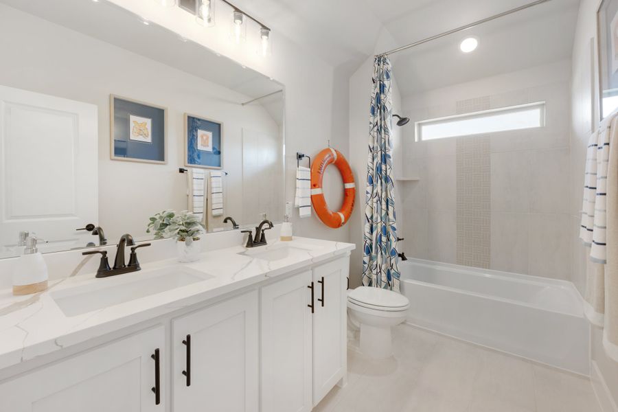 Bathroom with double white vanity, quartz countertop, and tub-shower combo with patterned curtain