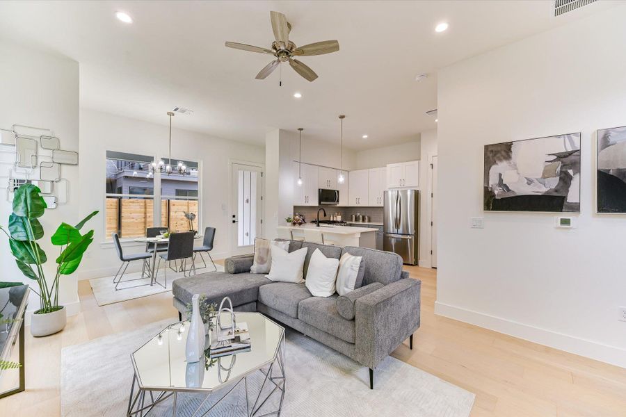 Welcome to an airy, light-filled sanctuary. The open-concept floor plan seamlessly connects the living, dining, and kitchen areas, anchored by warm blonde hardwoods and soaring ceilings.
